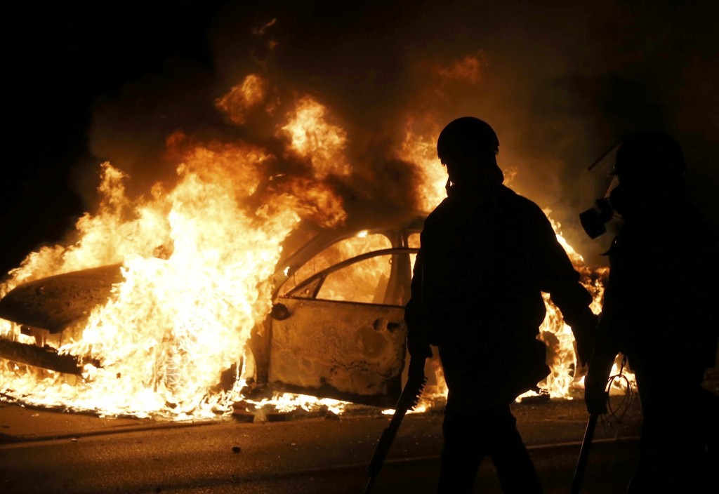 Police walk past a burning police car on the street after a grand jury returned no indictment in the shooting of Michael Brown in Ferguson, Missouri